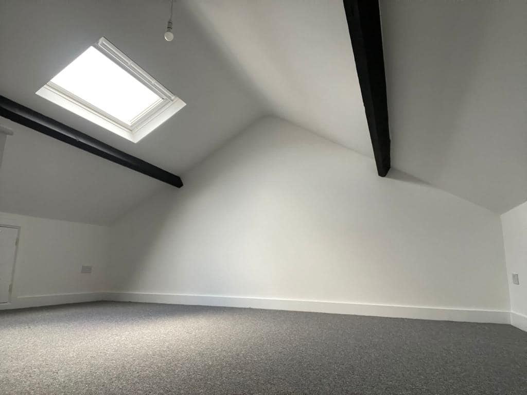 A finished white loft room with a roof window and dark beams