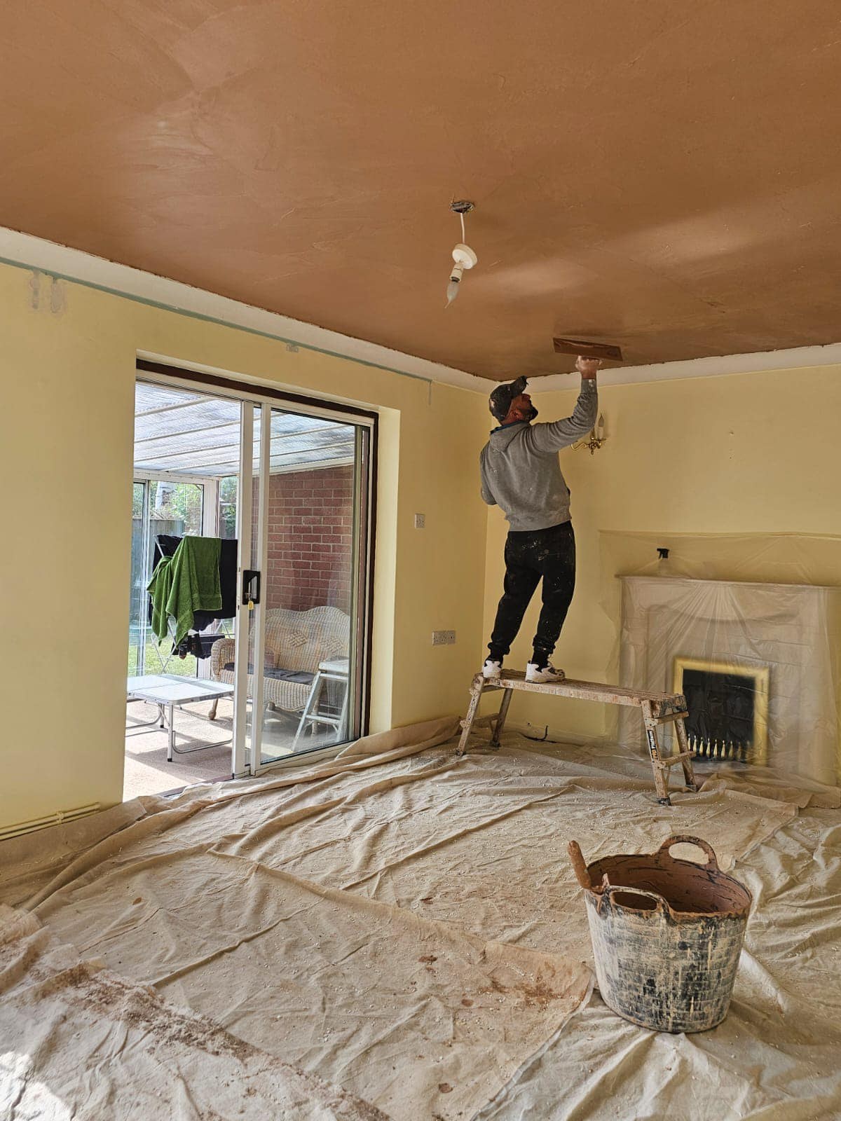 A Selba plasterer skimming a living room ceiling, with the floor sheeted
