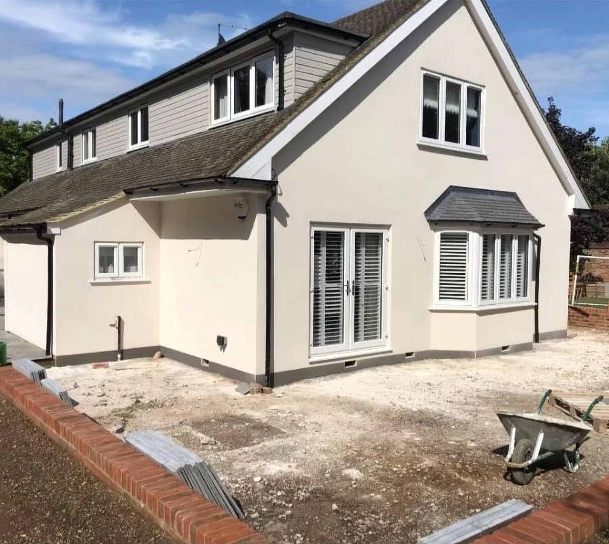 A cream rendered chalet bungalow just finished by Selba Plastering, with a wheelbarrow still on site