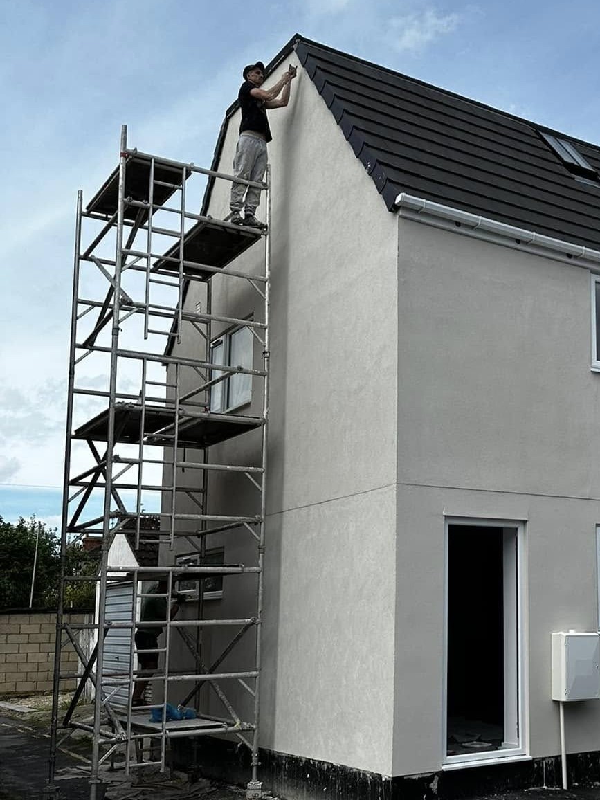 Grey rendered new build gable with a tower scaffold and one of our team at the top